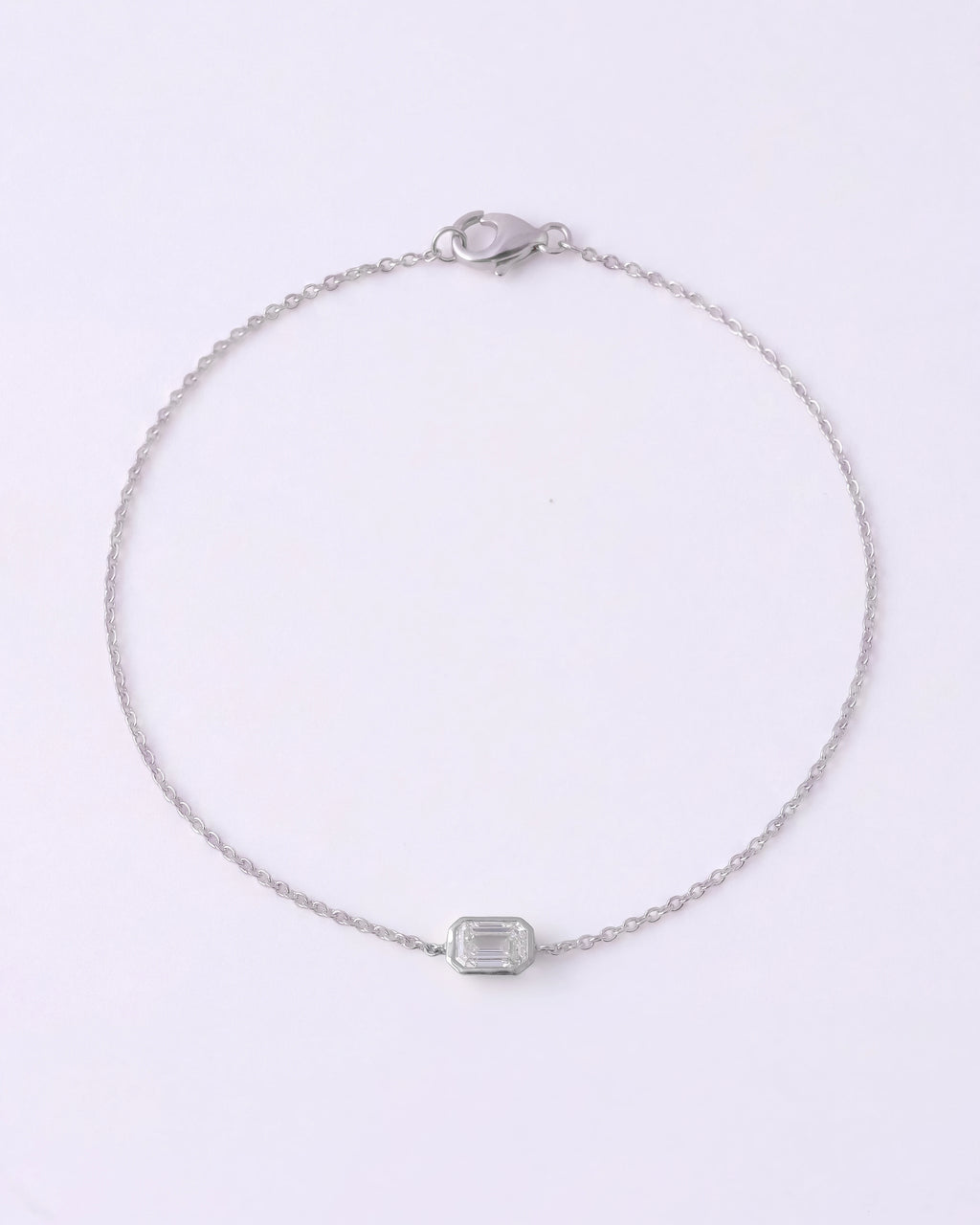 A delicate silver chain bracelet with a small rectangular clear gemstone centerpiece, displayed on a clean white background.