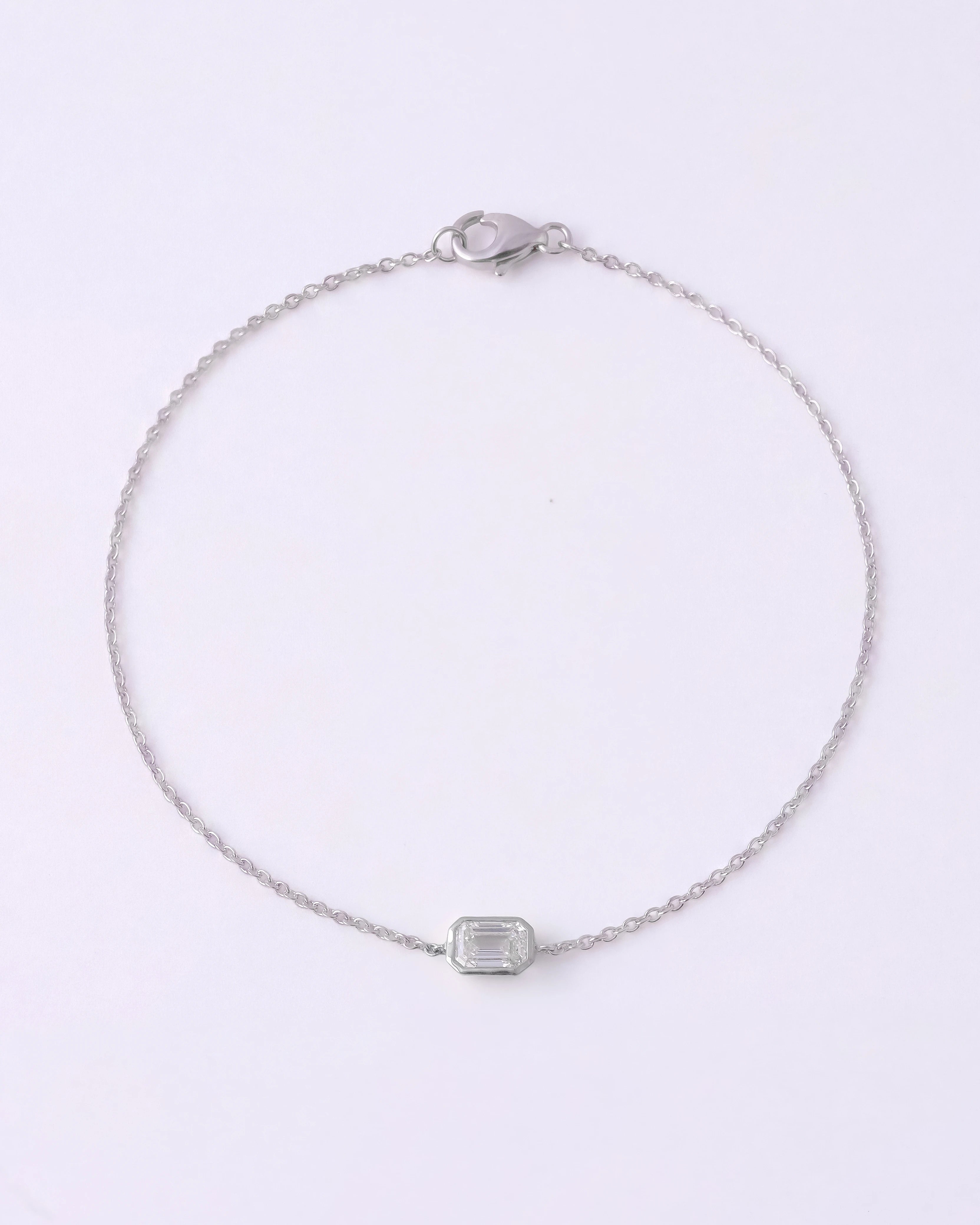 A delicate silver chain bracelet with a small rectangular clear gemstone centerpiece, displayed on a clean white background.