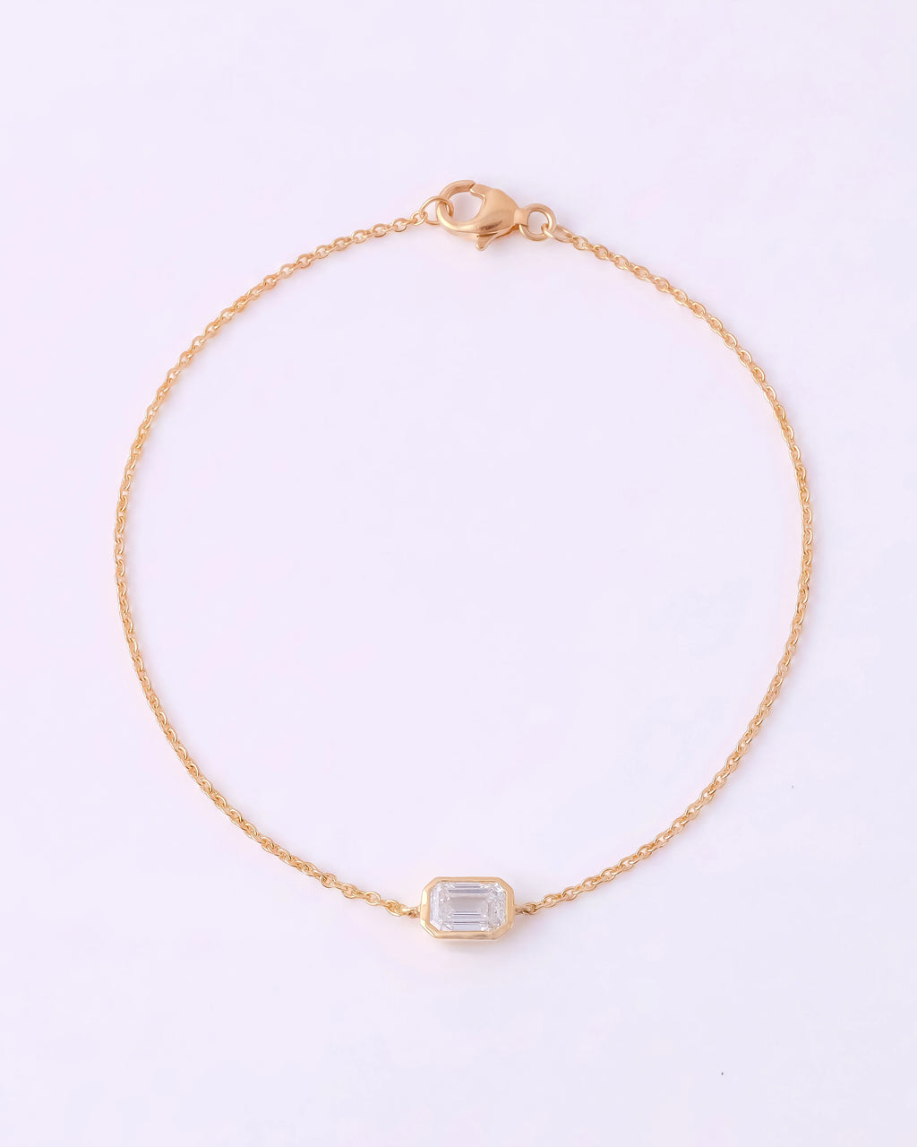 A delicate gold chain bracelet with a small rectangular bezel-set clear gemstone, displayed on a clean white background.