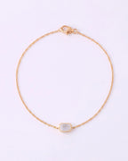 A delicate gold chain bracelet with a small rectangular bezel-set clear gemstone, displayed on a clean white background.