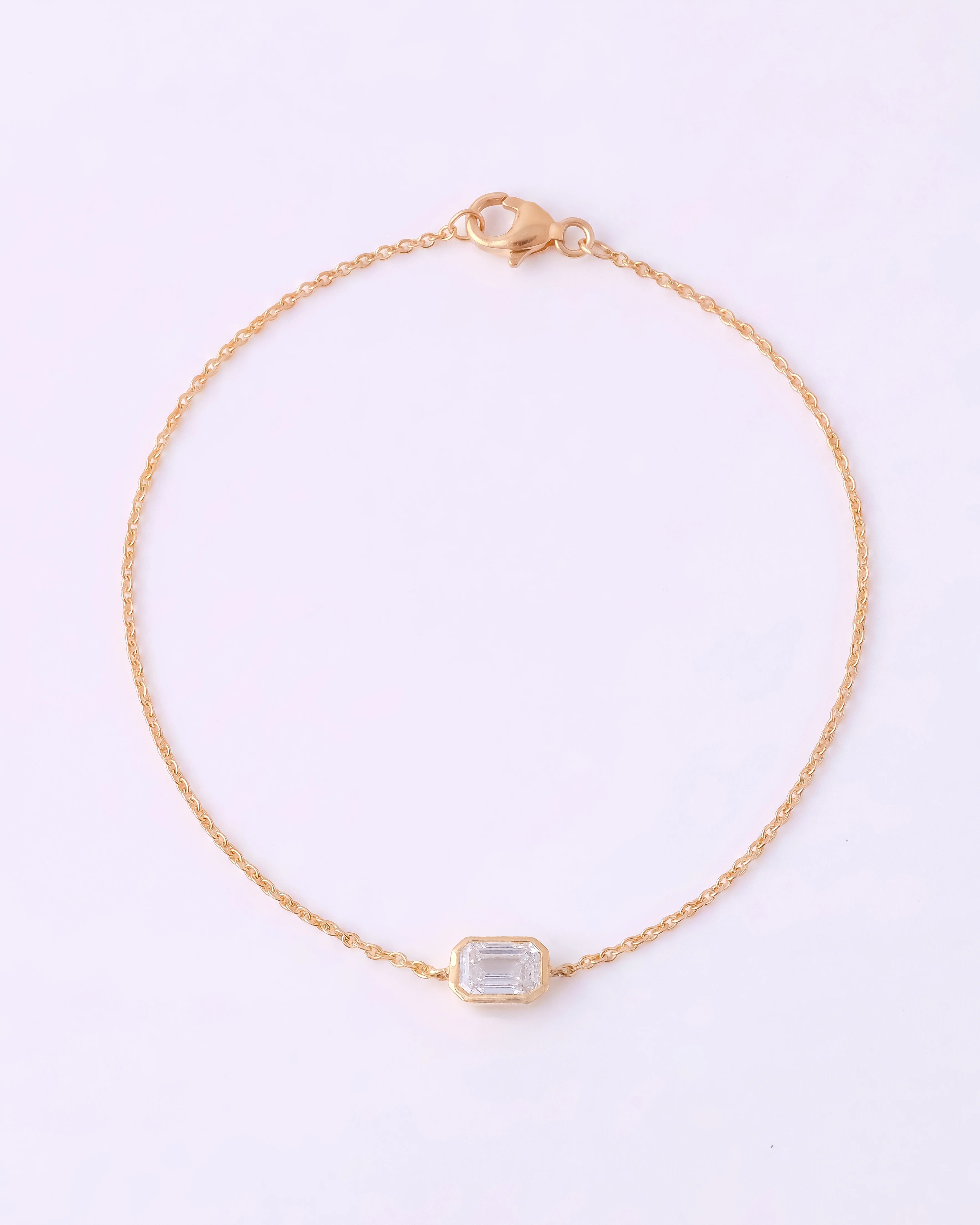 A delicate gold chain bracelet with a small rectangular bezel-set clear gemstone, displayed on a clean white background.