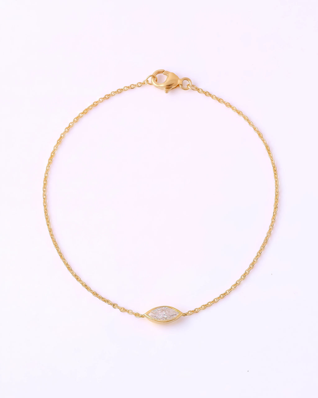A delicate yellow gold chain bracelet with a small marquise-shaped clear gemstone centerpiece, displayed on a clean white background.