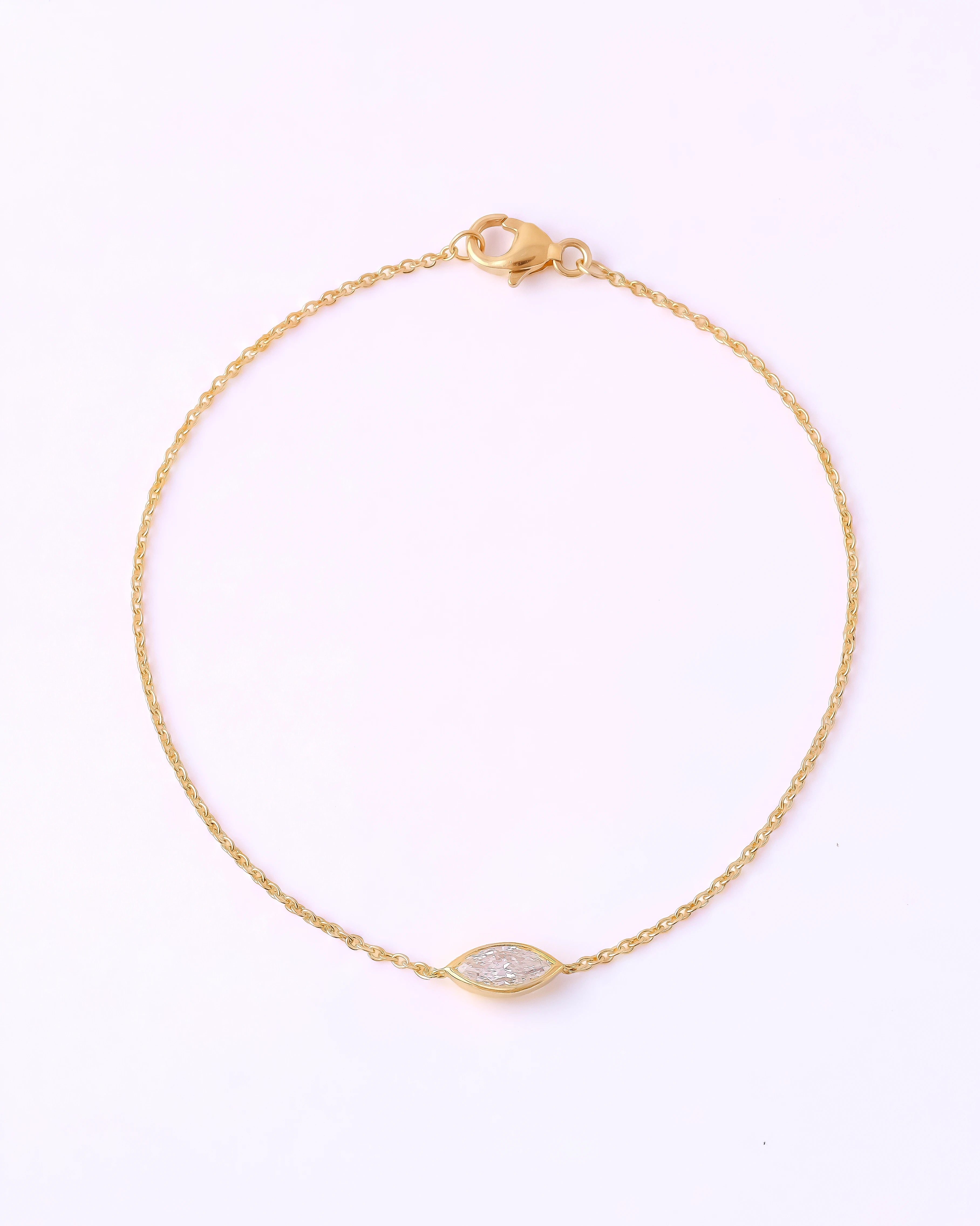 A delicate yellow gold chain bracelet with a small marquise-shaped clear gemstone centerpiece, displayed on a clean white background.