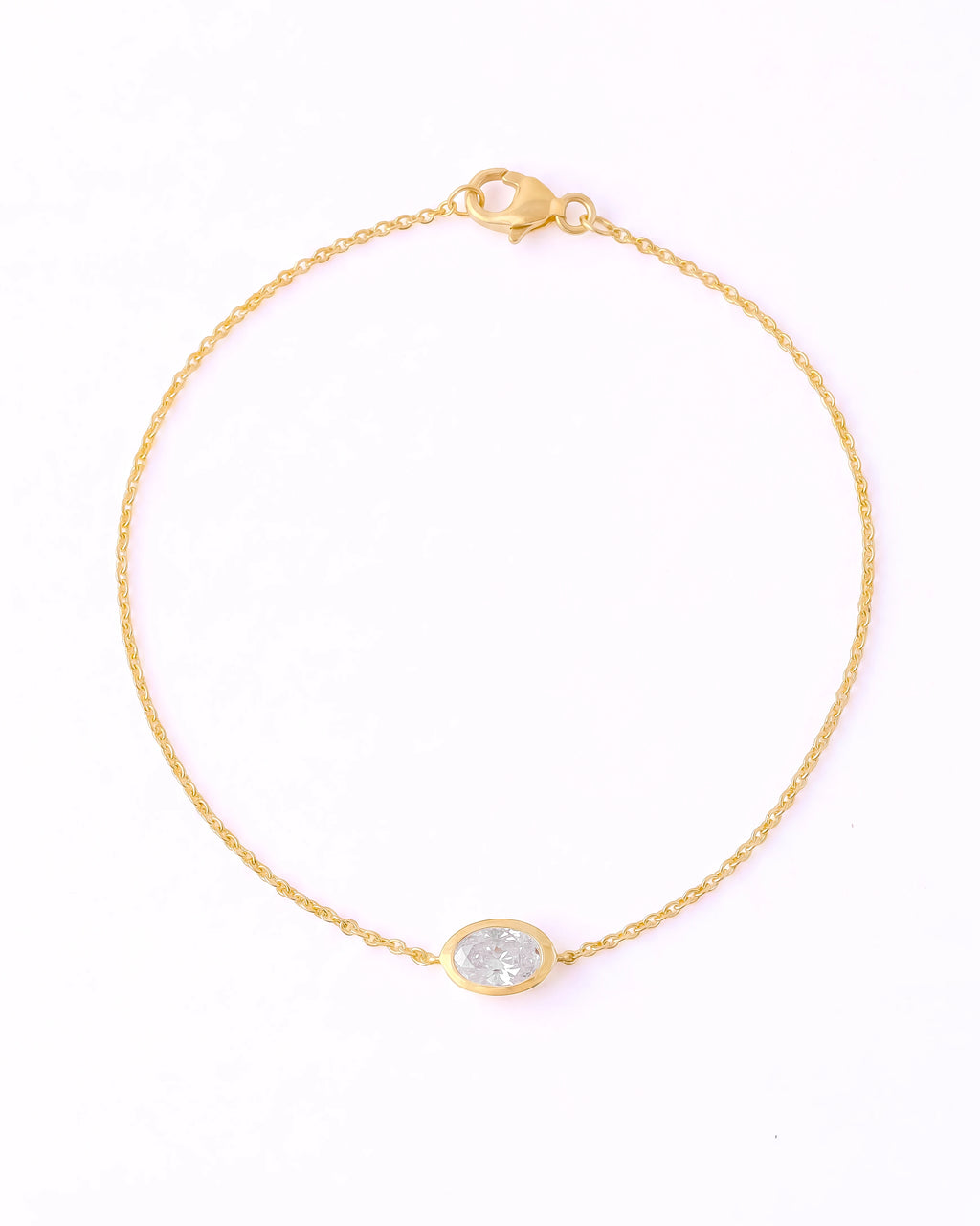 A delicate yellow gold chain bracelet with a small oval bezel-set clear stone, displayed on a clean white background.