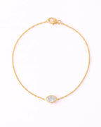 A delicate yellow gold chain bracelet with a small oval bezel-set clear stone, displayed on a clean white background.