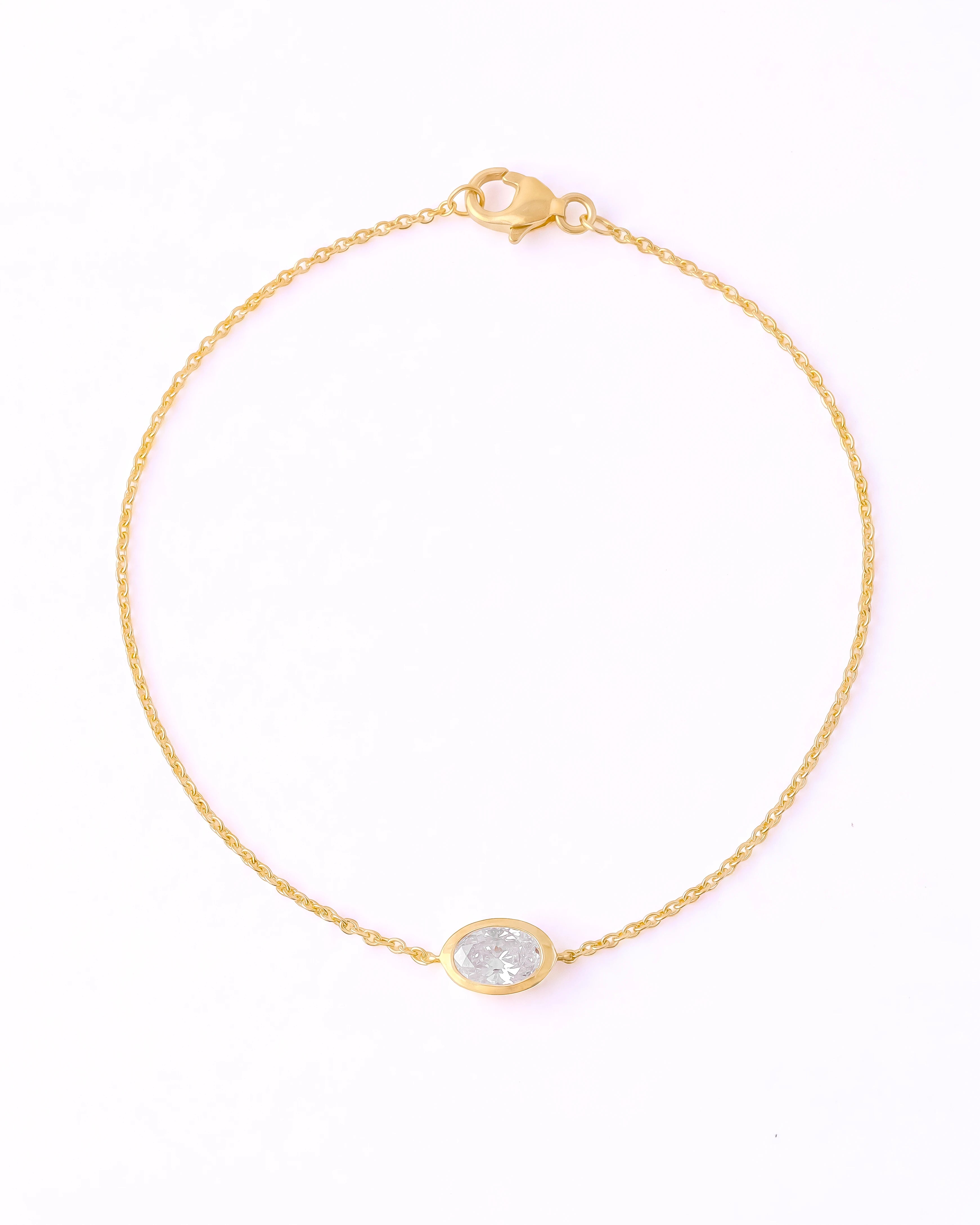 A delicate yellow gold chain bracelet with a small oval bezel-set clear stone, displayed on a clean white background.