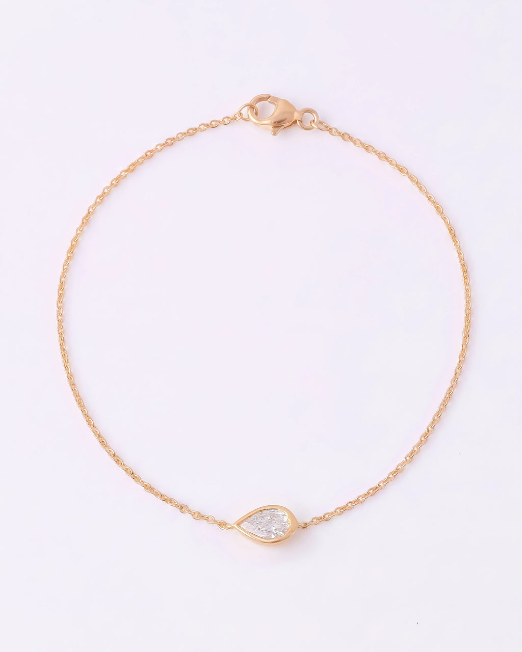 A delicate gold chain bracelet with a small teardrop-shaped clear gemstone pendant, displayed on a clean white background.