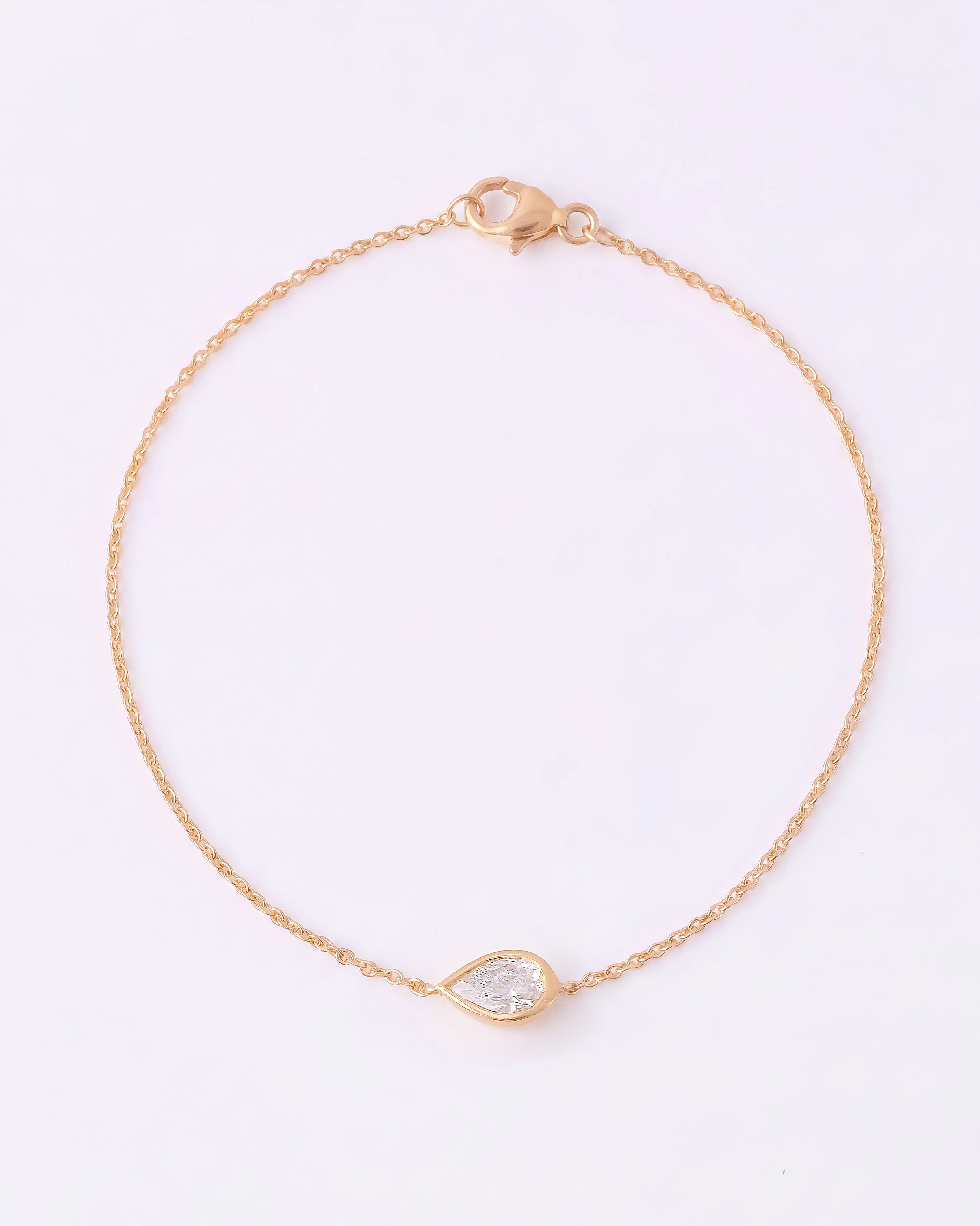 A delicate gold chain bracelet with a small teardrop-shaped clear gemstone pendant, displayed on a clean white background.
