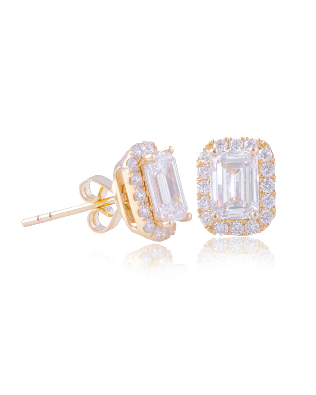 A pair of yellow gold halo stud earrings featuring large emerald-cut clear stones surrounded by smaller accent stones, shown on a clean white background with a soft reflection.